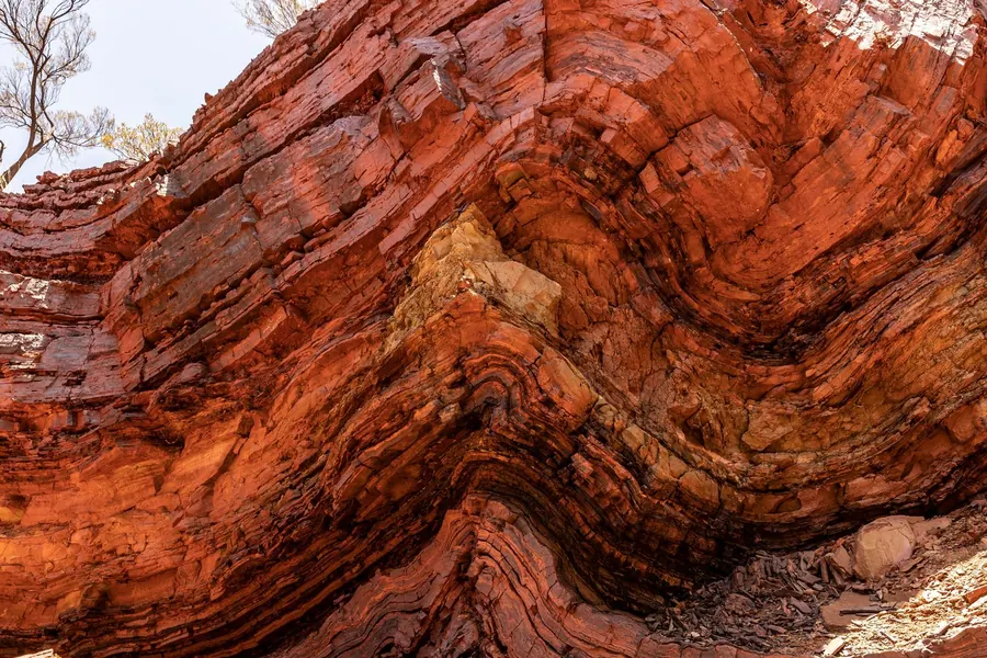Eine Felswand aus dünn geschichtetem Sediment; die Lagen sind scharf umgebogen und laufen als Paket weiter, unten Geröll.