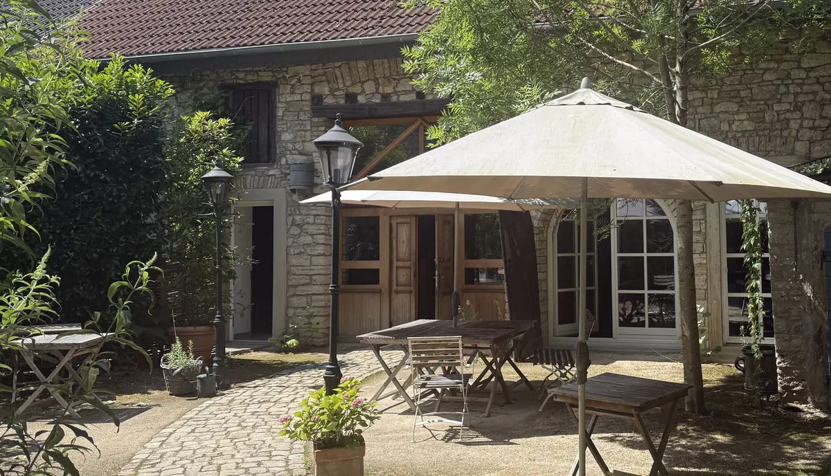 Der Innenhof des Alten Gutshofs an einem Sommertag: ein aufgespannter Sonnenschirm über runden Tischen, eine Laterne, efeubewachsene Mauern und Kopfsteinpflaster