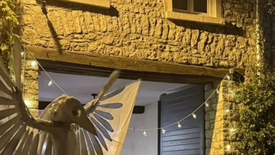 Die weiße Stelzenfigur im Ausschnitt: Kopf und Flügel vor der angestrahlten Bruchsteinfassade, darüber eine Lichterkette